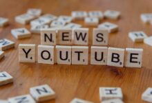 Scrabble tiles spelling words on wooden surface, focusing on YouTube and News.