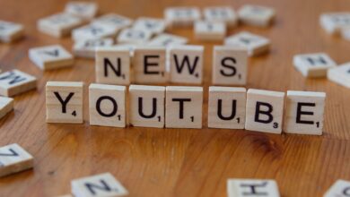 Scrabble tiles spelling words on wooden surface, focusing on YouTube and News.