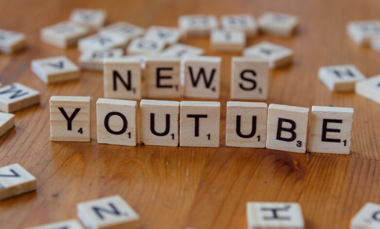 Scrabble tiles spelling words on wooden surface, focusing on YouTube and News.