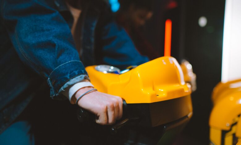 Hand holding handlebar of a yellow arcade racing game machine in a dimly lit setting.