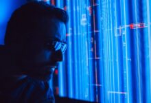A man in sunglasses intently studies a vibrant blue holographic screen, symbolizing digital technology.