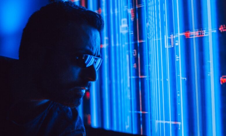 A man in sunglasses intently studies a vibrant blue holographic screen, symbolizing digital technology.