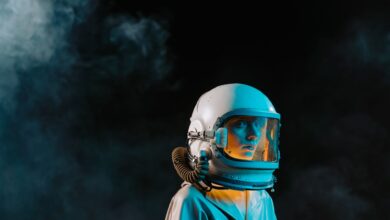 A dramatic portrait of a woman wearing a spacesuit and helmet in a dark, smoky setting.