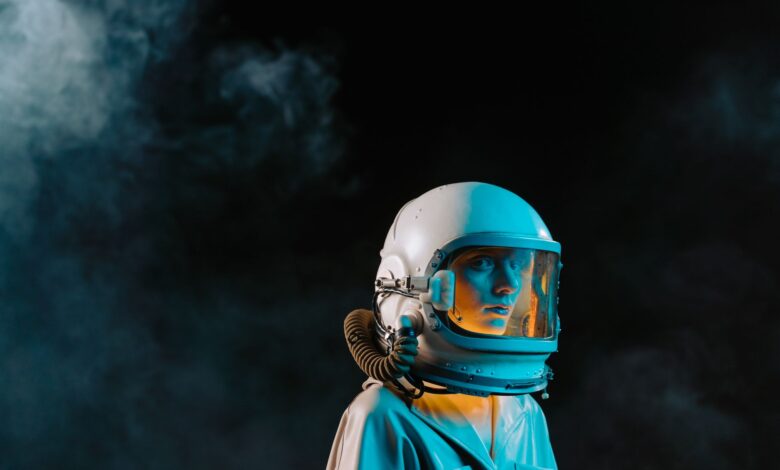 A dramatic portrait of a woman wearing a spacesuit and helmet in a dark, smoky setting.