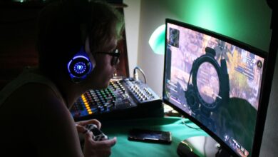 A dedicated gamer using a headset and controller while engrossed in a game, illuminated by green lights.