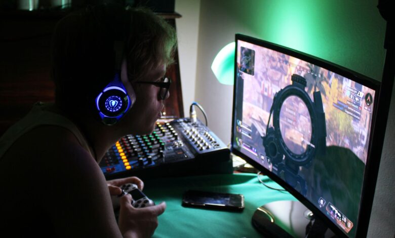 A dedicated gamer using a headset and controller while engrossed in a game, illuminated by green lights.