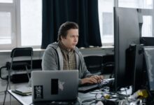 A dedicated programmer focused on coding at his workspace with dual monitors in a modern office setting.