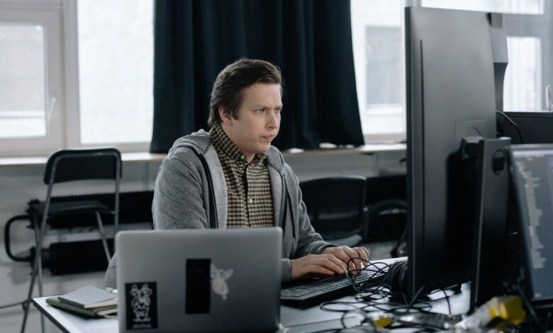 A dedicated programmer focused on coding at his workspace with dual monitors in a modern office setting.