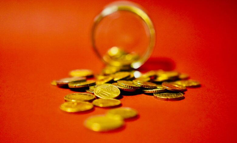 A collection of golden coins spilling from a glass jar on a vibrant red background symbolizes wealth.