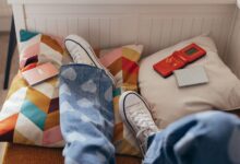 Teenager relaxes indoors with vintage games, colorful pillows, and casual jeans.
