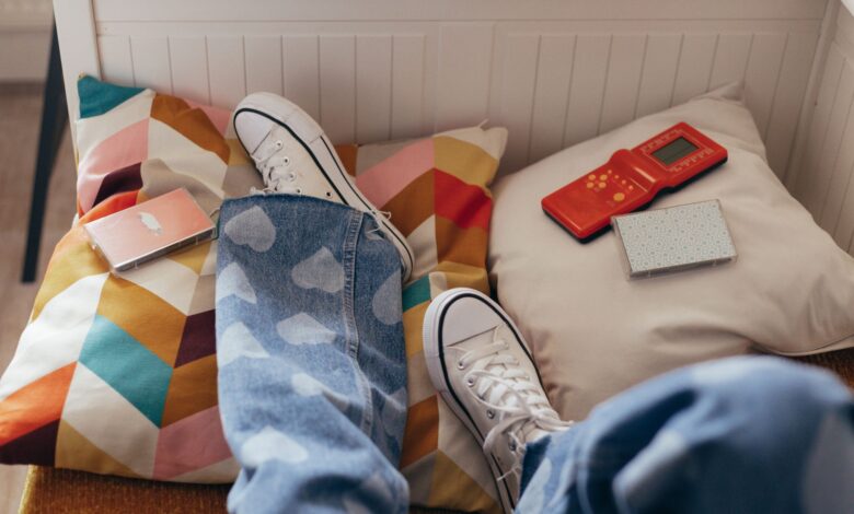 Teenager relaxes indoors with vintage games, colorful pillows, and casual jeans.