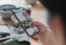 Close-up of a hand holding a smartphone browsing food recipes. Cozy kitchen setting.