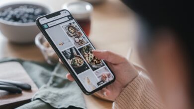 Close-up of a hand holding a smartphone browsing food recipes. Cozy kitchen setting.