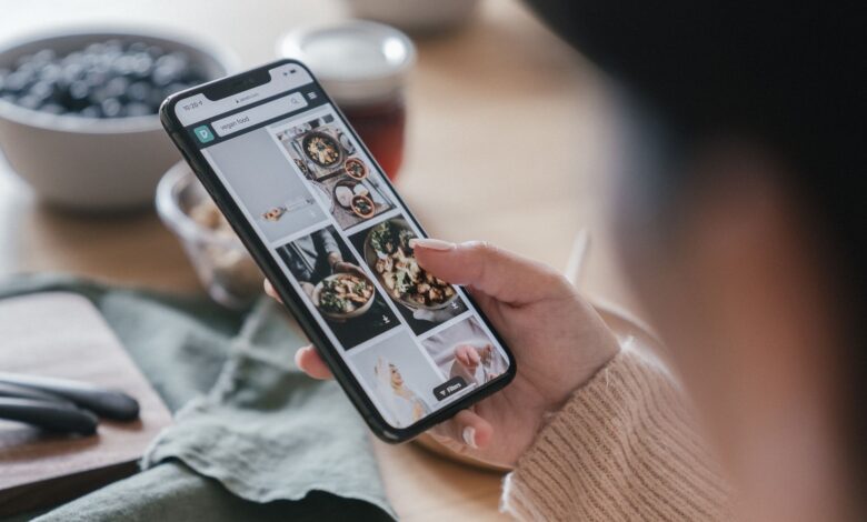 Close-up of a hand holding a smartphone browsing food recipes. Cozy kitchen setting.
