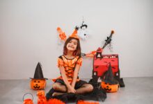 Cute child in a witch costume with Halloween decor, pumpkins, and festive backdrop.