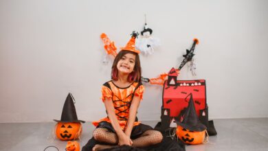 Cute child in a witch costume with Halloween decor, pumpkins, and festive backdrop.