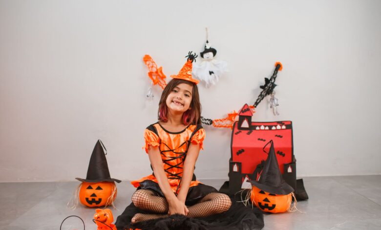 Cute child in a witch costume with Halloween decor, pumpkins, and festive backdrop.
