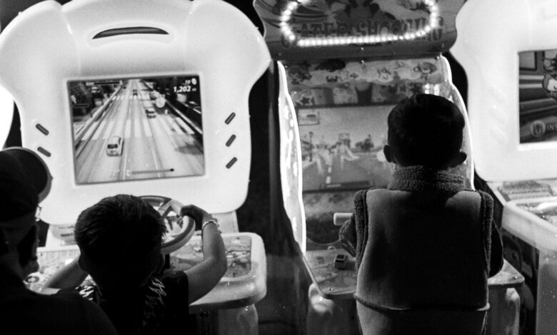Black and white photo of children playing arcade games, creating a nostalgic feel.