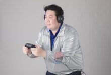 A man wearing headphones and a silver jacket engrossed in playing video games indoors.