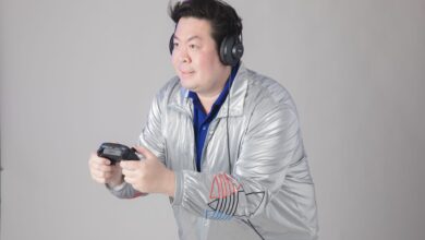 A man wearing headphones and a silver jacket engrossed in playing video games indoors.