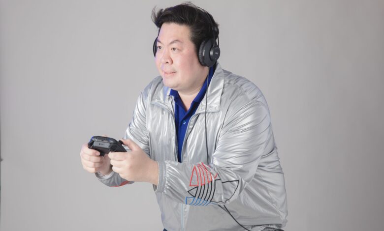 A man wearing headphones and a silver jacket engrossed in playing video games indoors.