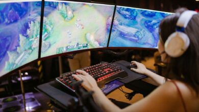A young woman intently gaming on a multi-screen setup, showcasing vibrant gaming visuals.