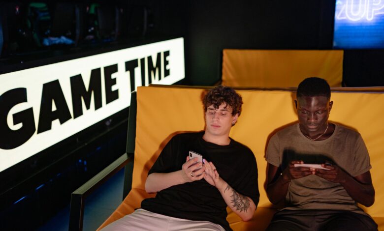 Two friends gaming on smartphones in a cozy indoor setting, enjoying leisure time together.