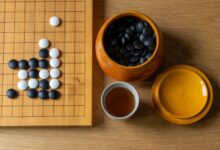 Top view of a Go board with black and white stones, tea, and bowls on a wooden surface.
