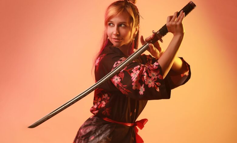 A woman in colorful cosplay posing with a samurai sword in a studio setting.