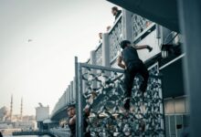 Children climbing a metal railing on a bridge, with a city mosque in background at day.