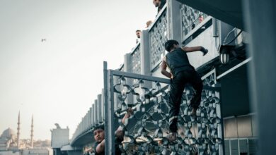 Children climbing a metal railing on a bridge, with a city mosque in background at day.