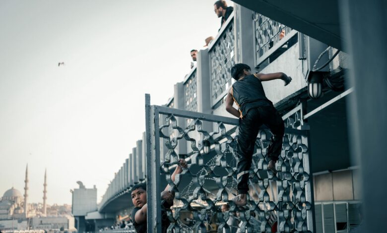 Children climbing a metal railing on a bridge, with a city mosque in background at day.