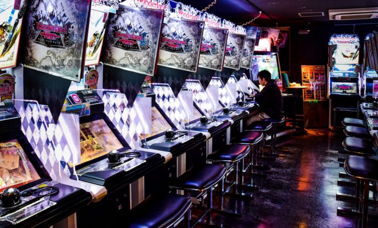 A man plays inside a modern arcade in Tokyo, illuminated by neon lights and gaming machines.