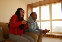 A couple engaged in playing video games, sitting on a sofa in a cozy living room setting.