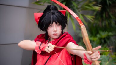 Young cosplayer dressed as an archer in a red costume poses outdoors.