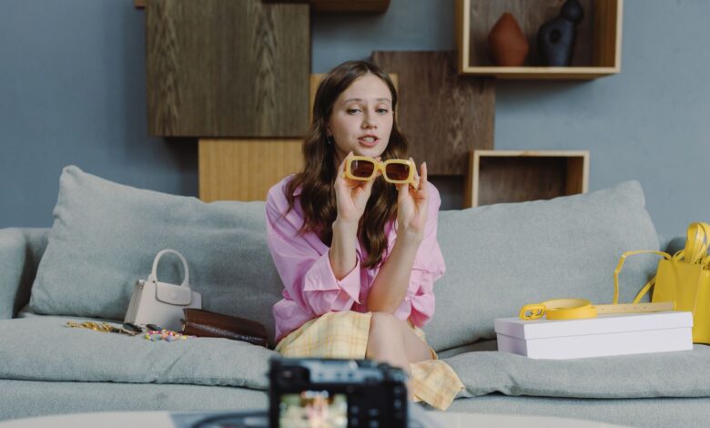 Young woman showcasing trendy sunglasses on a video blog at home.