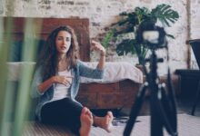 Woman sitting on floor filming vlog, discussing engaging topic. Home setting with cozy atmosphere.