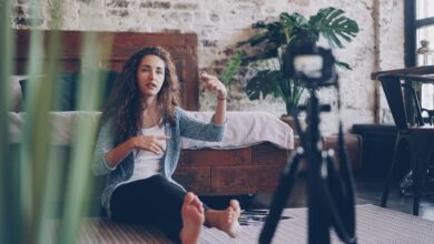 Woman sitting on floor filming vlog, discussing engaging topic. Home setting with cozy atmosphere.