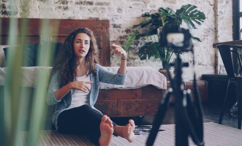 Woman sitting on floor filming vlog, discussing engaging topic. Home setting with cozy atmosphere.