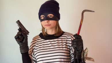 A woman dressed as a robber holding a gun and crowbar, implying criminal activity.