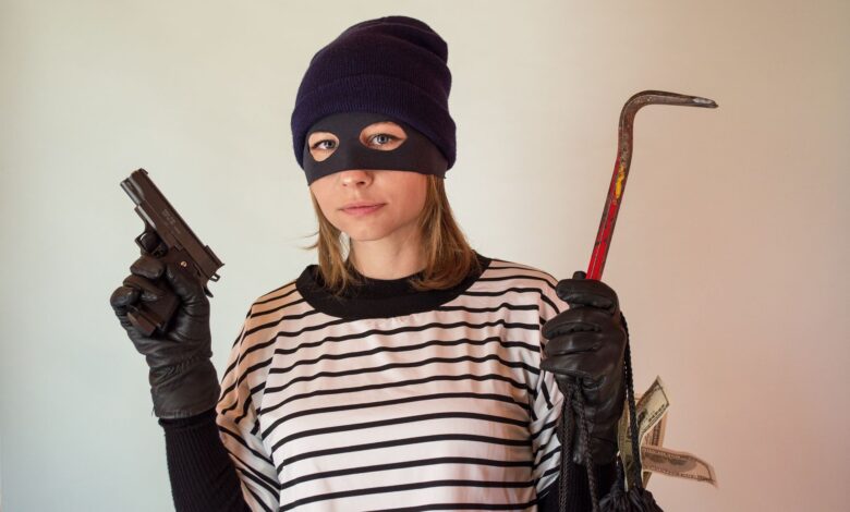 A woman dressed as a robber holding a gun and crowbar, implying criminal activity.