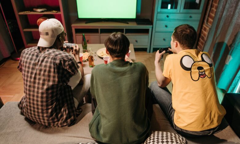 Three young men enjoying a home gaming session together, playing video games in a cozy indoors setting.