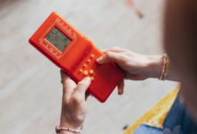 Hands holding a retro red handheld game console, playing a classic game.