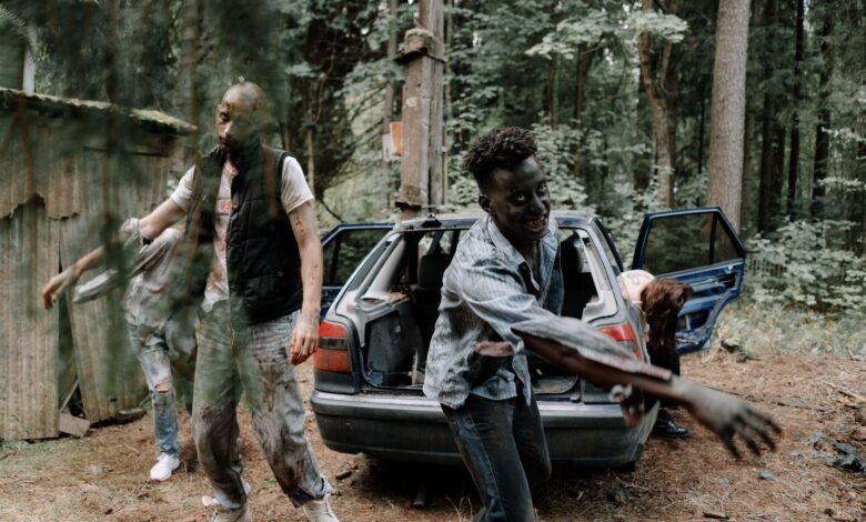 A group of zombies walking near an abandoned car in a creepy forest setting.