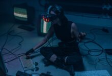A woman in a VR headset and gloves interacts with technology in a dimly lit room.