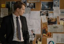 Detective in suit examining evidence on cork board during investigation process.