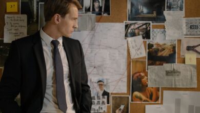 Detective in suit examining evidence on cork board during investigation process.