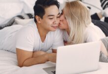 A couple shares a loving moment while browsing on a laptop in their bedroom, highlighting modern relaxation.