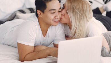 A couple shares a loving moment while browsing on a laptop in their bedroom, highlighting modern relaxation.