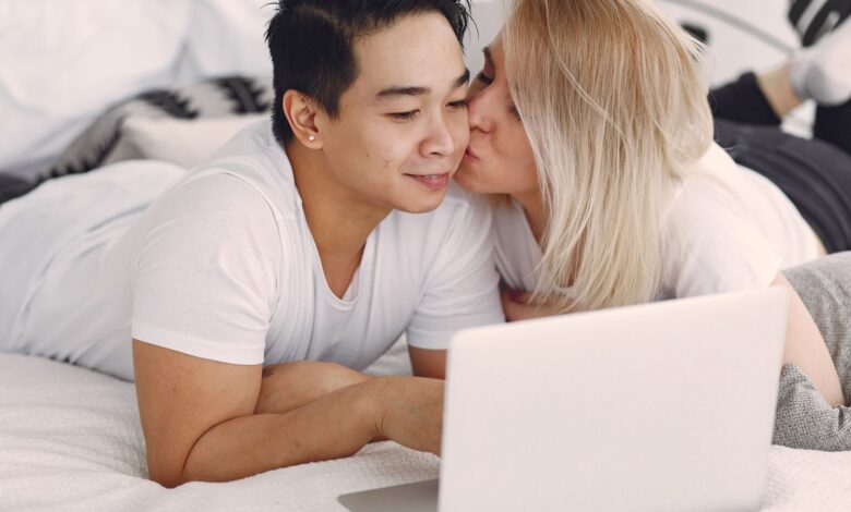A couple shares a loving moment while browsing on a laptop in their bedroom, highlighting modern relaxation.